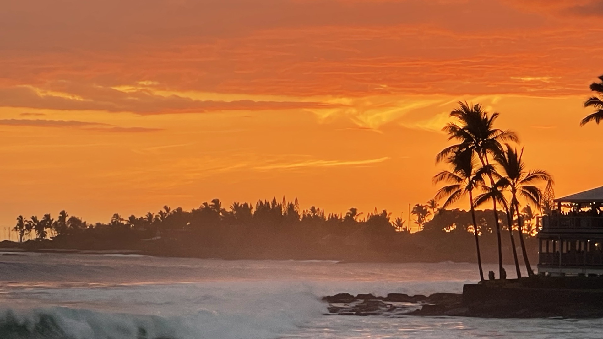 Kailua Kona sunset — fiery sky over the Pacific, palm silhouettes along the coastline